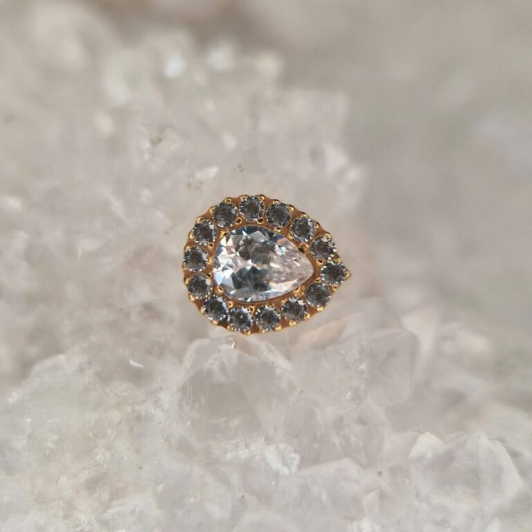 Bijou de piercing doré en forme de goutte, pierre centrale entourée de petits zircons, disponible au salon Jolie Piqûre à Arles
