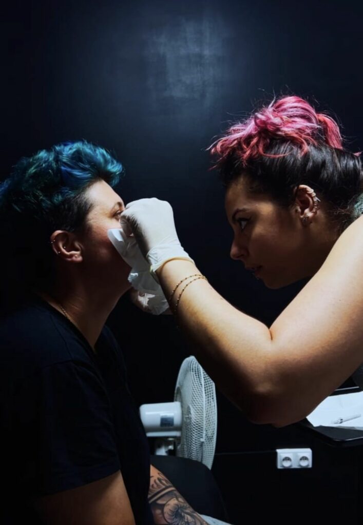 Pierceuse gantée préparant la peau d’une cliente avant un piercing du visage au salon Jolie Piqûre à Arles