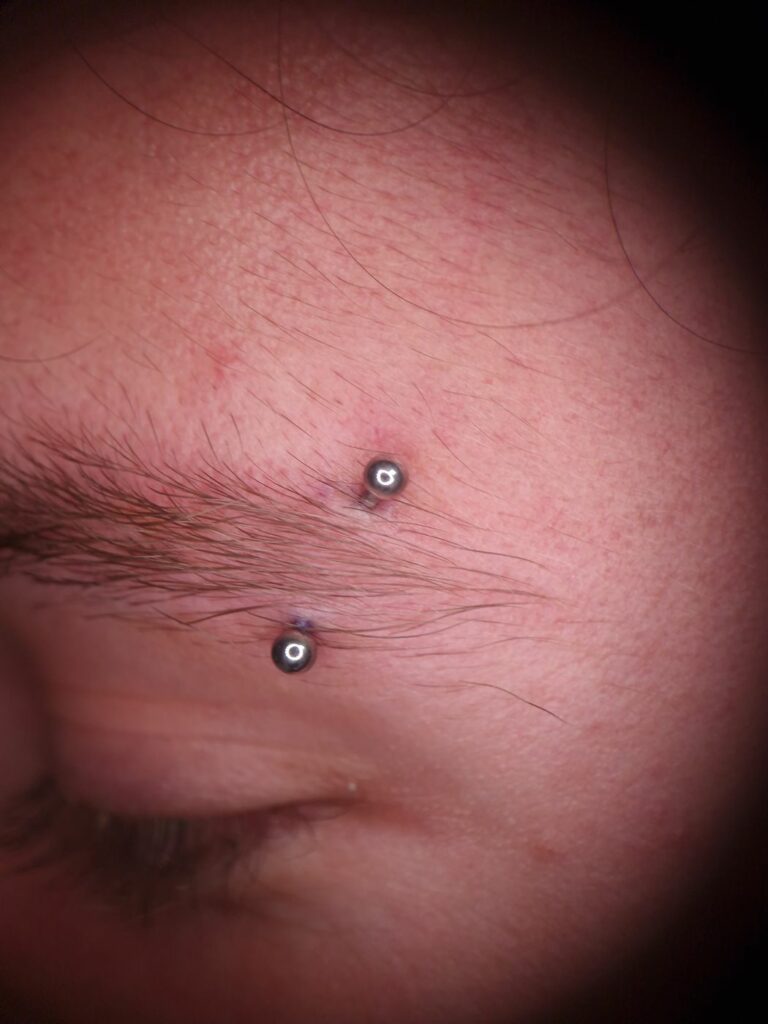 Piercing arcade (sourcil) avec barre courbe et billes en titane, réalisé par Oc Piercing au salon Jolie Piqûre à Arles
