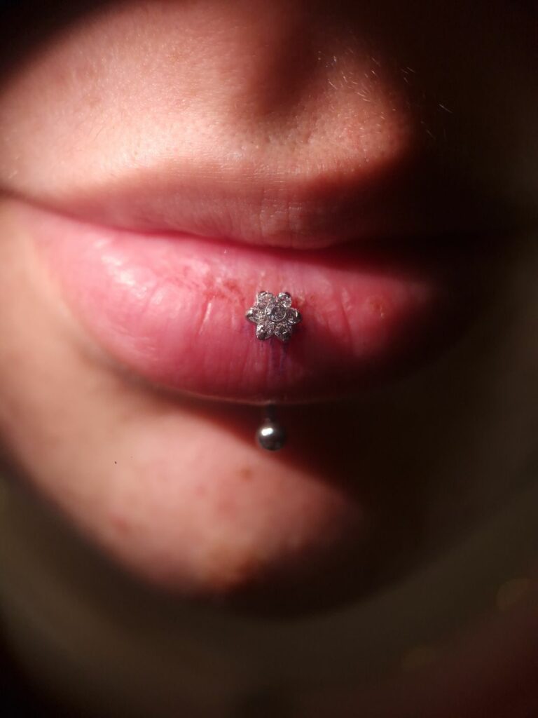 Piercing labret vertical sur la lèvre inférieure avec embout fleur en zircons, réalisé par Oc Piercing au salon Jolie Piqûre à Arles