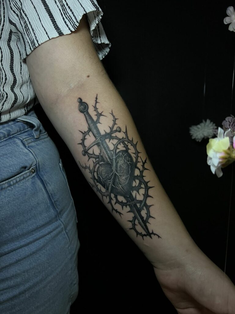 Tatouage noir sur l’avant-bras : cœur anatomique transpercé d’un poignard et entouré de ronces épineuses, réalisé à Arles