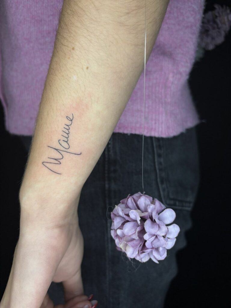 Tatouage lettering fineline du mot « Maman » en écriture manuscrite sur l’avant-bras, réalisé au salon Jolie Piqûre à Arles