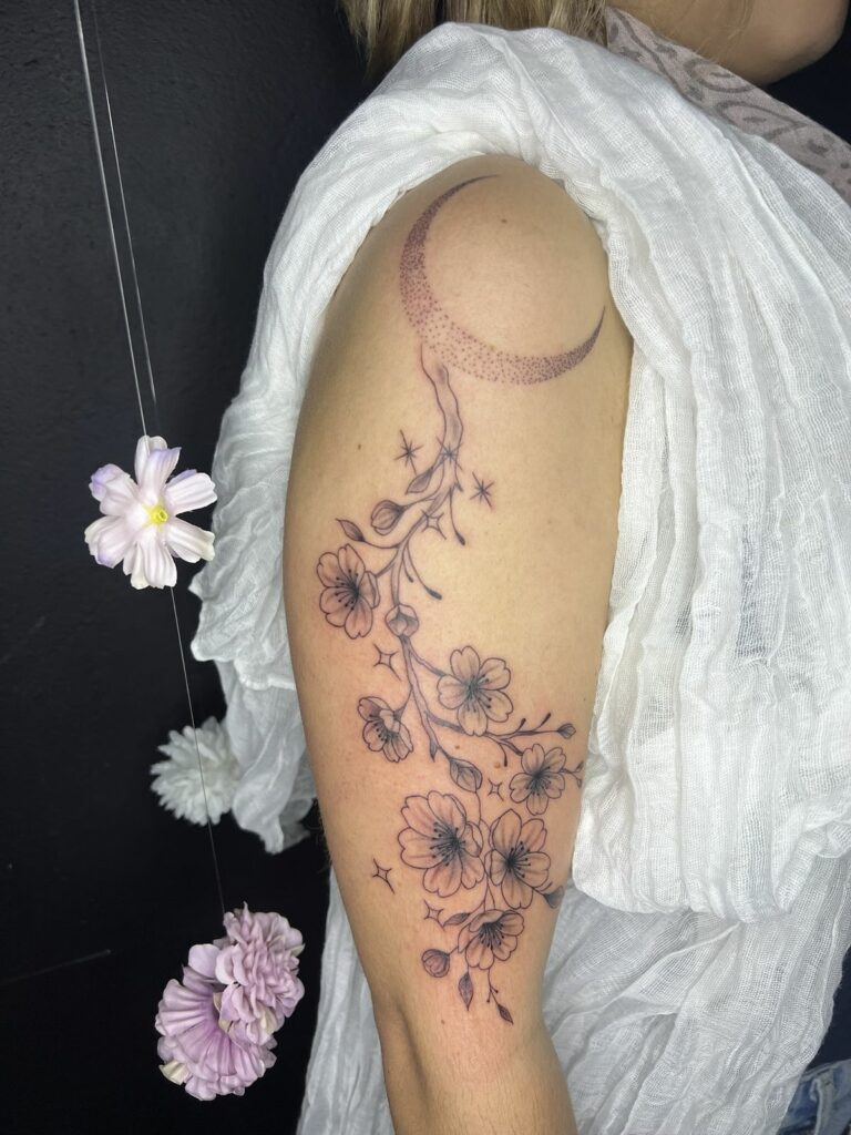Tatouage sur le bras : croissant de lune en dotwork d’où descend une branche de cerisier en fleurs avec des étoiles, réalisé à Arles
