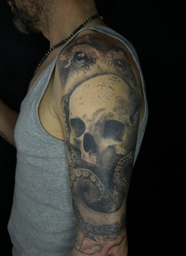 Tatouage réaliste noir et gris sur le bras et l’épaule : crâne enlacé par les tentacules d’une pieuvre, réalisé au salon Jolie Piqûre à Arles