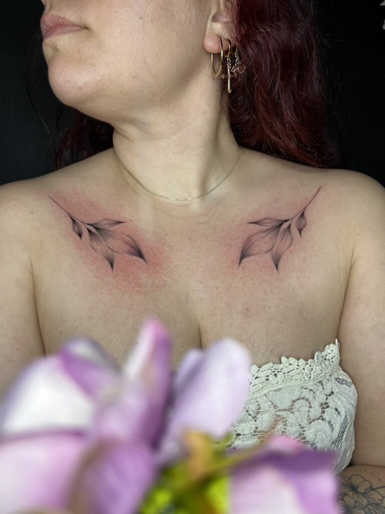Tatouage fineline symétrique de feuillages sur les deux clavicules, ombrages doux, réalisé au salon Jolie Piqûre à Arles