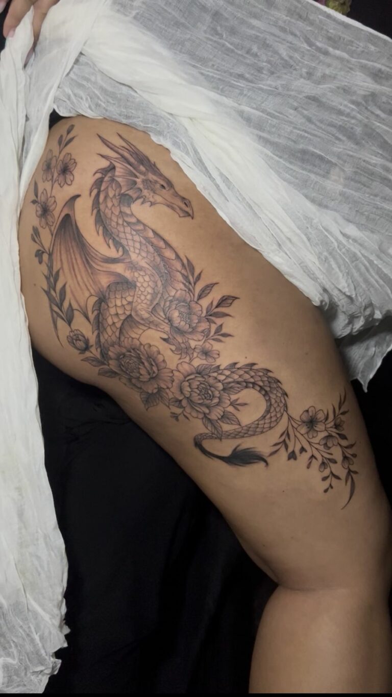 Grand tatouage noir et gris sur la cuisse : dragon aux écailles détaillées entouré de pivoines et de fleurs de cerisier, réalisé à Arles