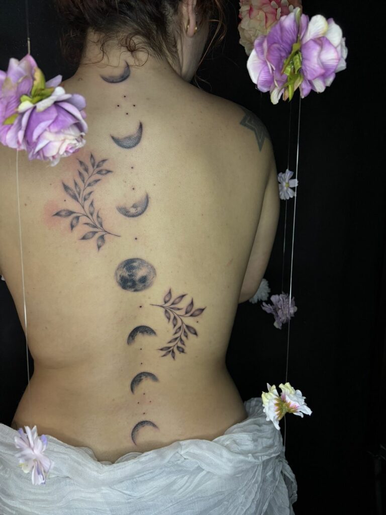 Tatouage le long de la colonne vertébrale : phases de la lune en dotwork entre deux branches de feuillage, réalisé au salon Jolie Piqûre à Arles